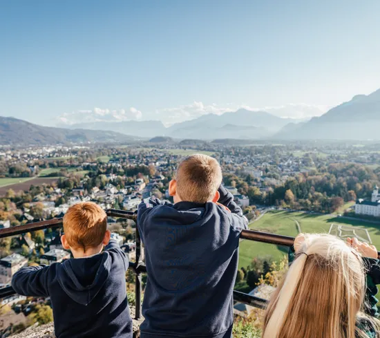 Kinder blicken von einem Aussichtspunkt auf Stadt und Berglandschaft